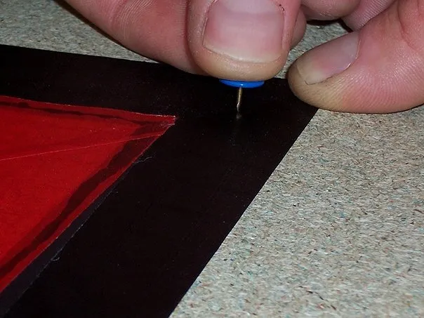 Fixation d'une aile avec des punaises. (Les trous ne posent pas de problème car ce contour noir de 3 cm sera replié 2 fois pour faire un ourlet/contour noir de 1cm tout autour de la voile.)